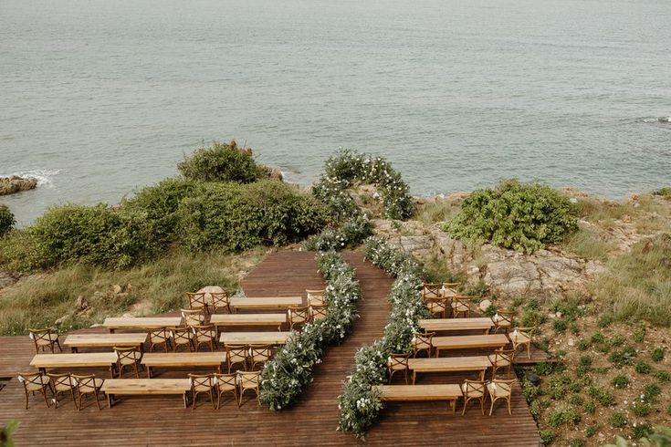 rows of wooden benches sitting on top of a wooden deck next to the ocean with greenery