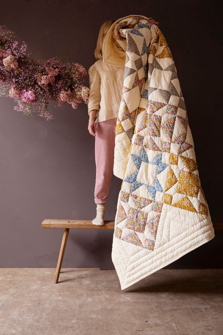 a woman is standing on a bench with a quilt draped over her head and flowers in front of her