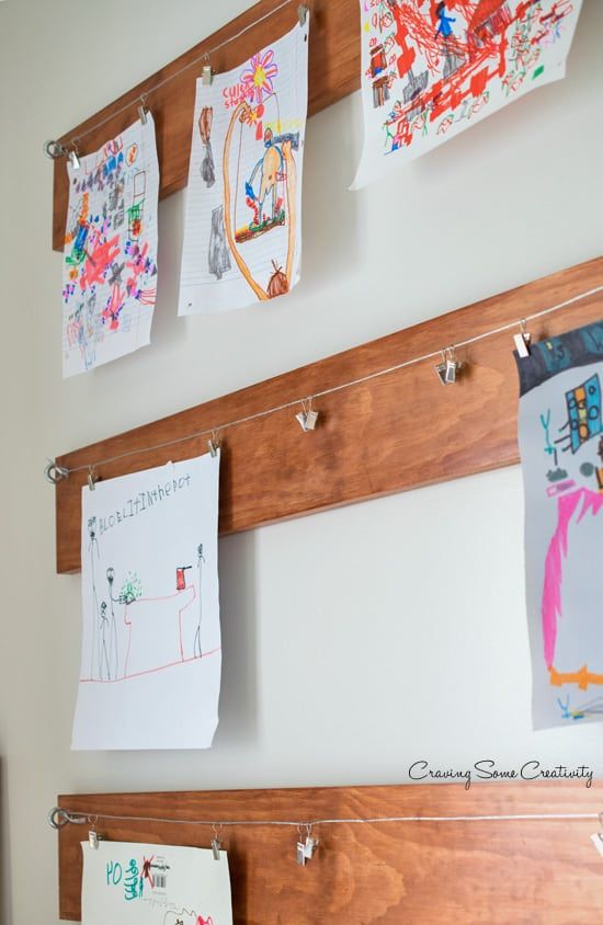 several children's drawings are hanging on the wall next to clothes pins and magnets