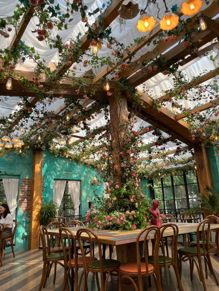 a dining room with tables and chairs covered in vines, hanging lights and flowers on the ceiling