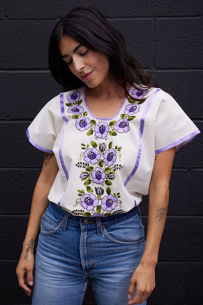 A heritage piece in our collection, this hand embroidered floral blouse from Oaxaca in a vibrant lilac is a best selling silhouette. Over a lightweight cotton, accented in bright ribbons this  slightly vintage in feeling that works perfectly within a modern wardrobe. 100% cotton gauze ONE SIZE (RECOMMENDED FOR SIZES XS Cotton Floral Print Blouse For Festival, Bohemian Purple Blouse For Spring, Purple Bohemian Blouse For Spring, Purple Casual Embroidered Top For Spring, Purple Floral Embroidery Top For Spring, Casual Purple Embroidered Top For Spring, Spring Cotton Tops With Boho Collar, Spring Cotton Blouse With Boho Collar, Spring Festival Cotton Blouse