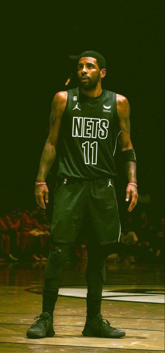 a man standing on top of a basketball court wearing a black jersey and green pants