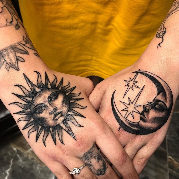 two hands with sun and moon tattoos on their palms, one holding the other's hand