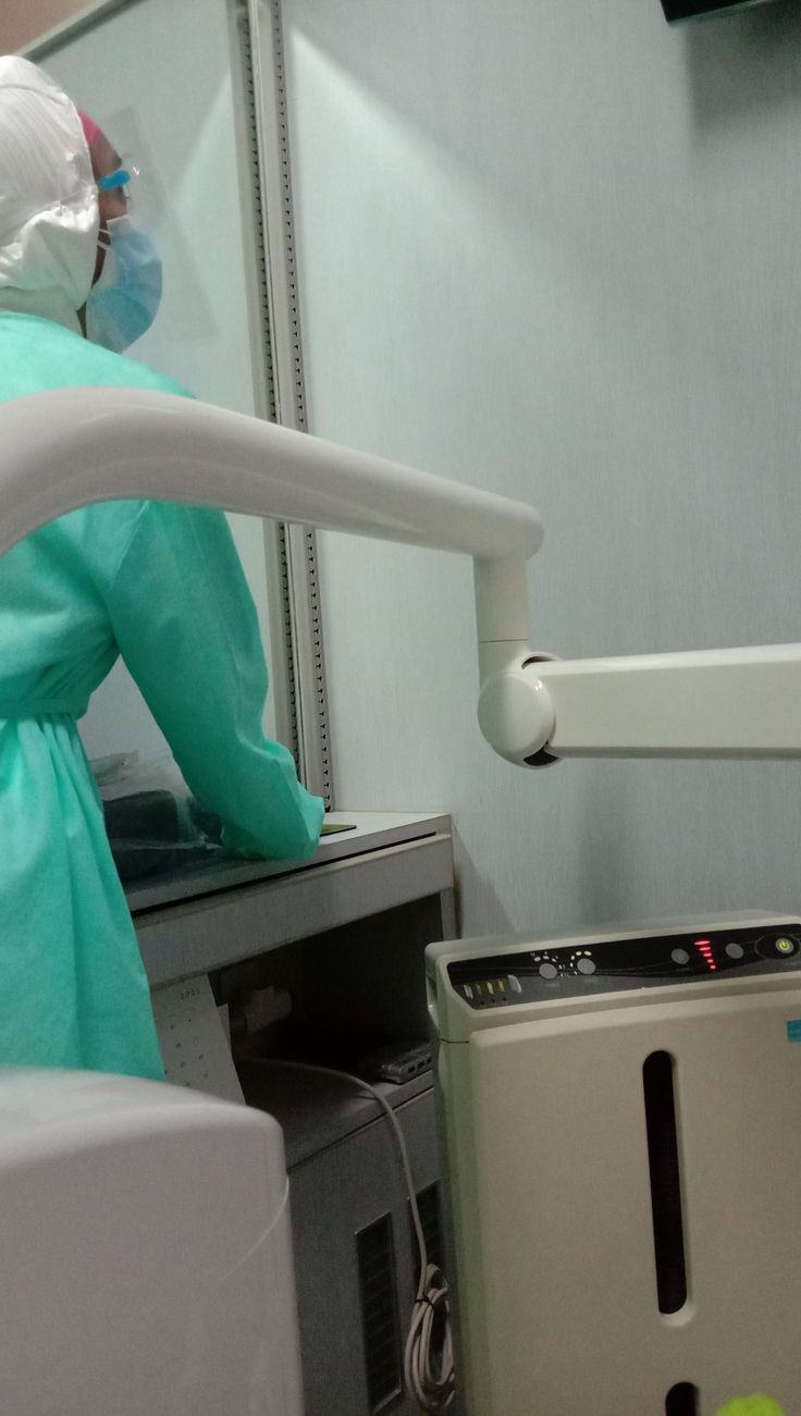 a person wearing a surgical mask and gown standing next to a machine in a room