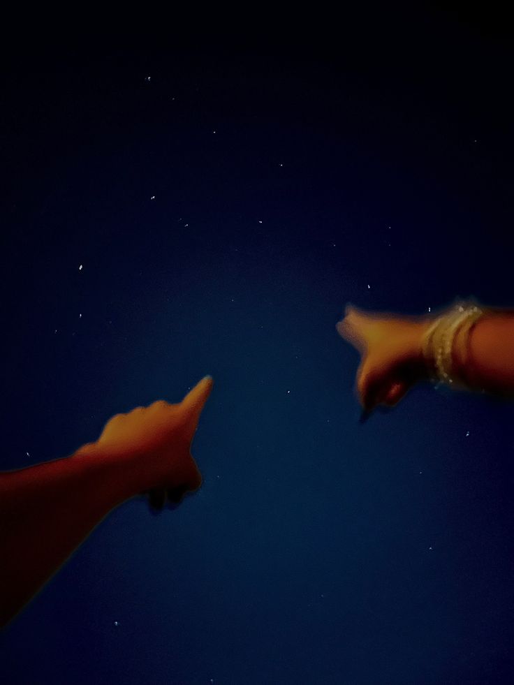 two hands reaching towards each other in the dark sky at night with stars behind them