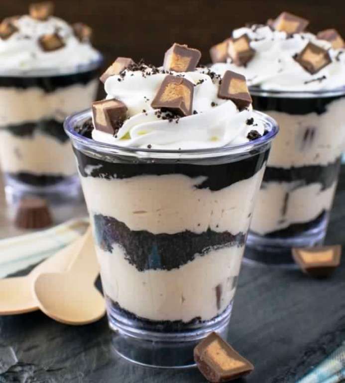 two desserts in plastic cups with chocolate and marshmallows on top, sitting on a table