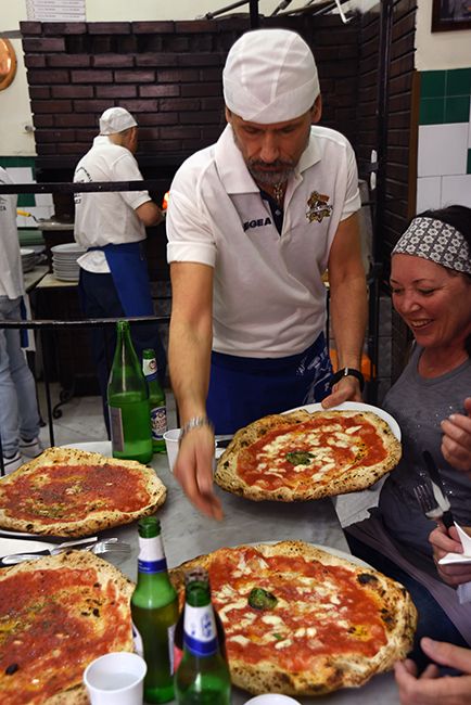 a group of people standing around a table with pizzas on it