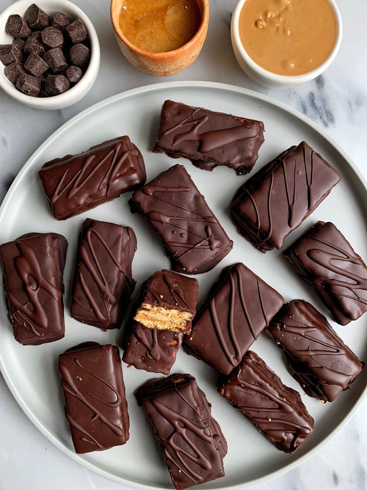 there are many pieces of chocolate on the plate and two bowls with peanut butter in them