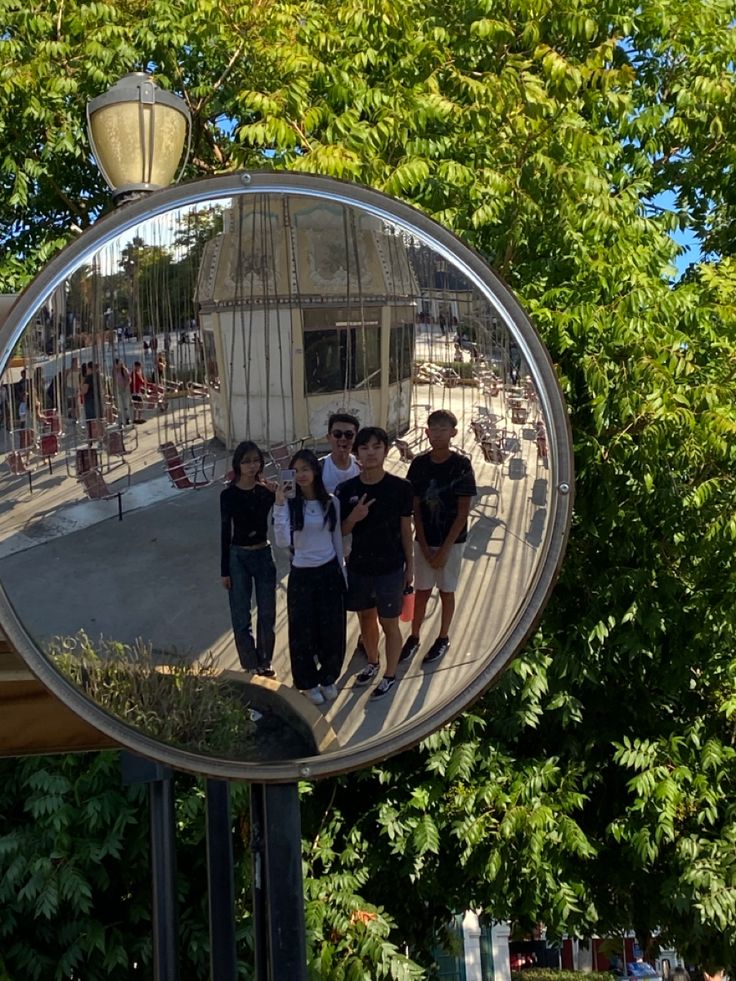 a group of young people standing in front of a large mirror on a street corner