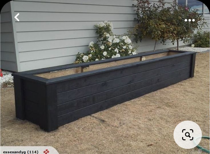 a planter box with flowers in it on the ground next to a building and a hose