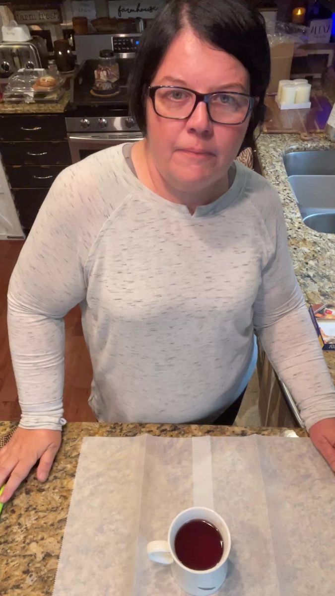 a woman sitting at a kitchen counter with a cup of coffee in front of her