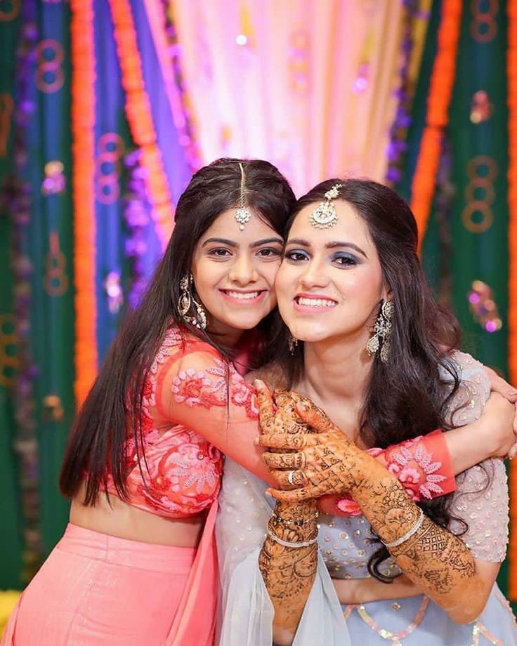 two young women hugging each other in front of colorful lights and garlands on the wall