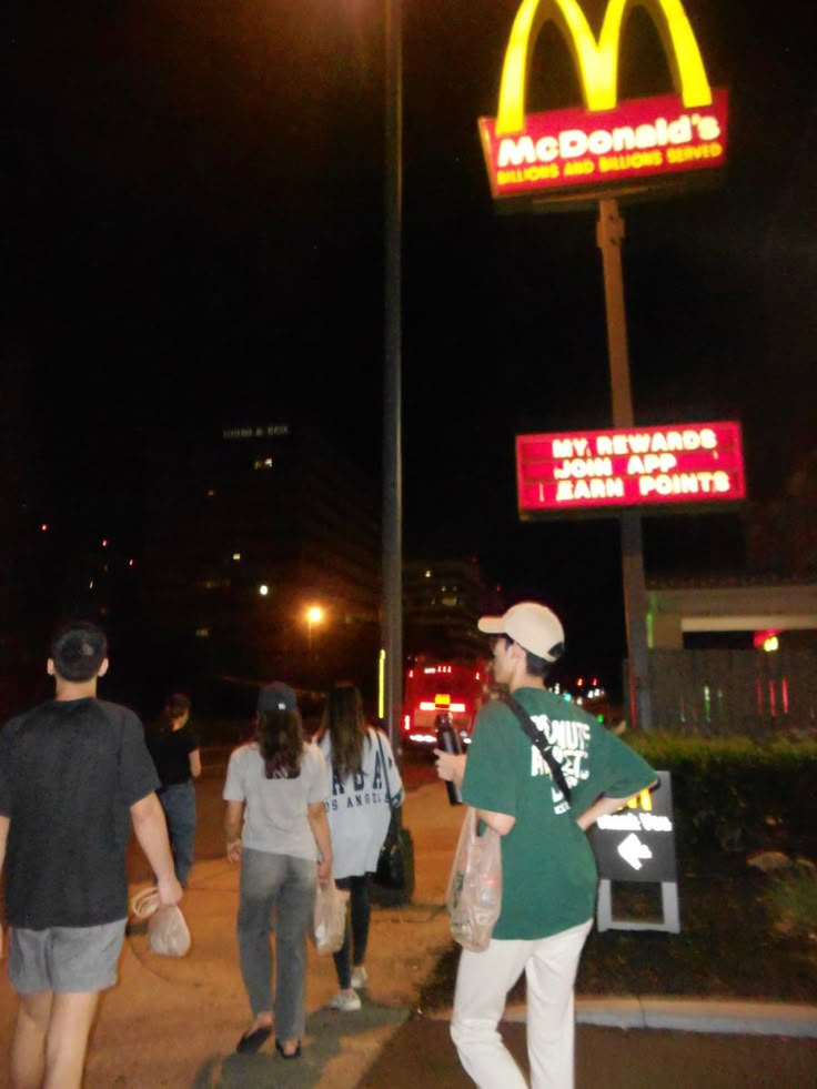 people walking down the sidewalk in front of a mcdonald's restaurant at night time