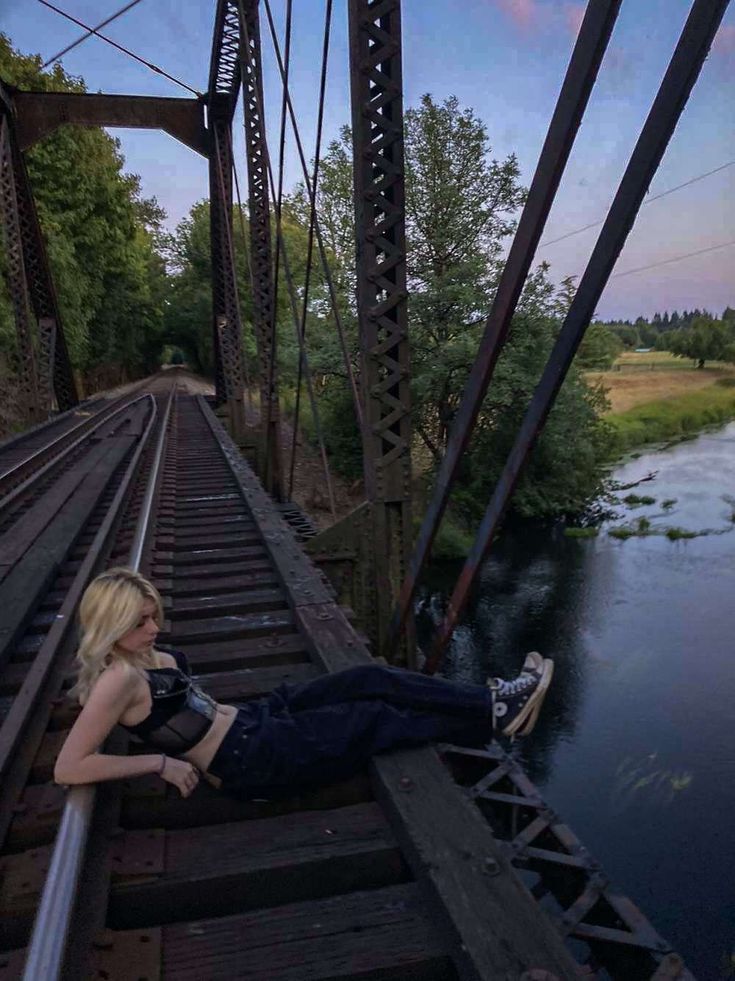 a woman laying on top of a train track next to a river