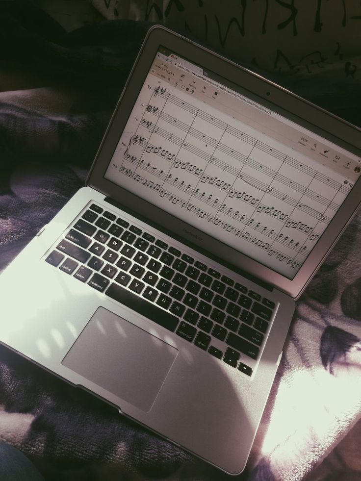 an open laptop computer sitting on top of a bed covered in sheet music sheets and notes