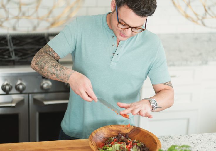 a man cutting vegetables in a wooden bowl