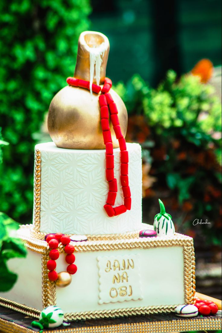 a white and gold cake sitting on top of a table in front of green plants