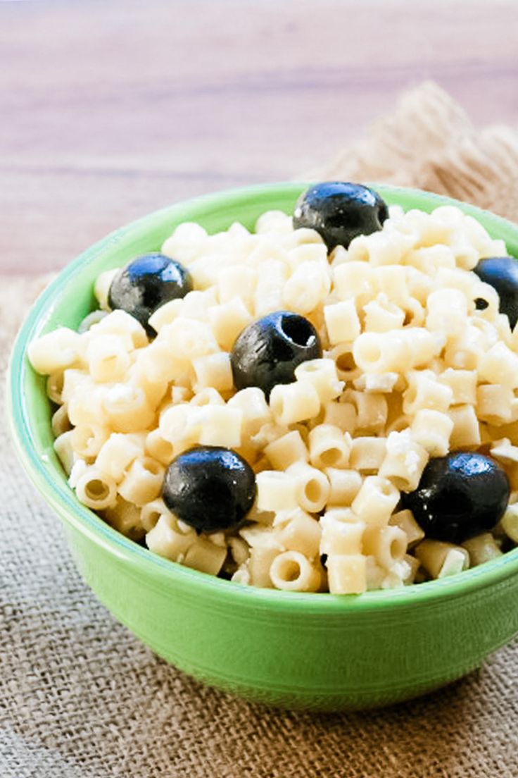 a green bowl filled with macaroni and blueberries on top of a table