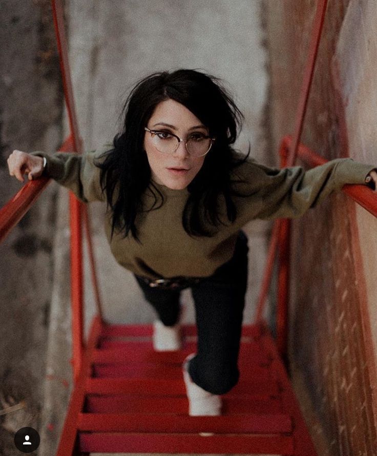 a woman with glasses is walking down the stairs and looking at the camera while holding her arms out