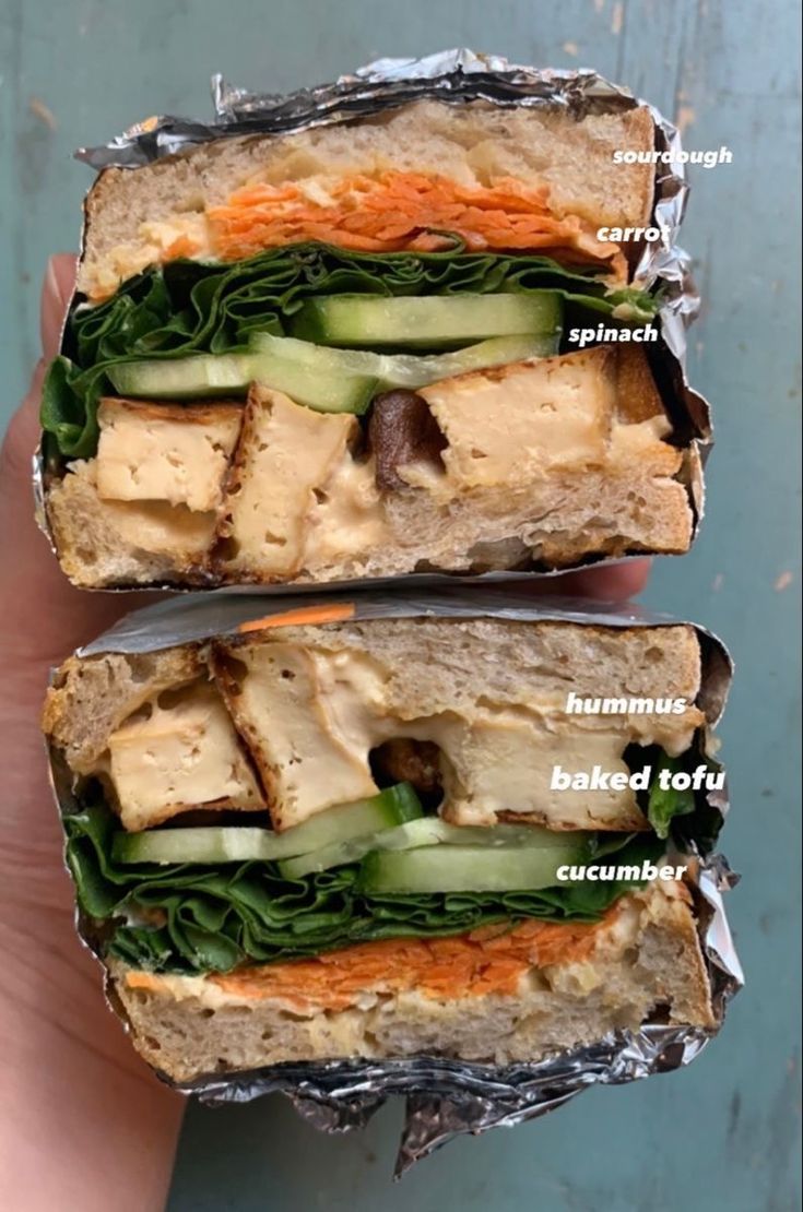 two sandwiches with different types of meat and vegetables in wrappers on top of each other