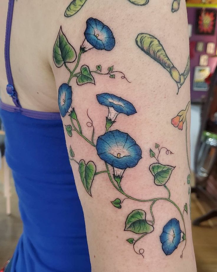 a woman's arm with blue flowers and green leaves on the left side of her body