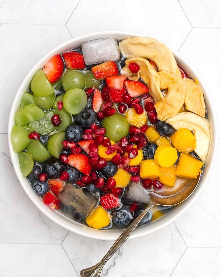 a white bowl filled with lots of different types of fruit next to a spoon on top of a table