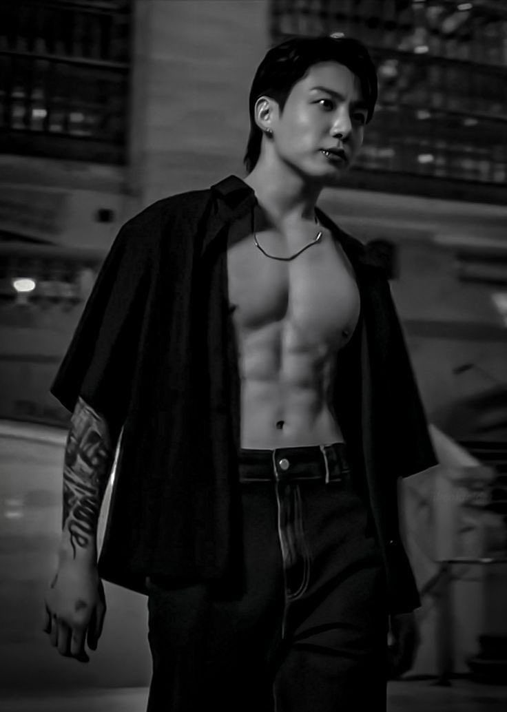 a shirtless man walking down the street in black and white with tattoos on his chest