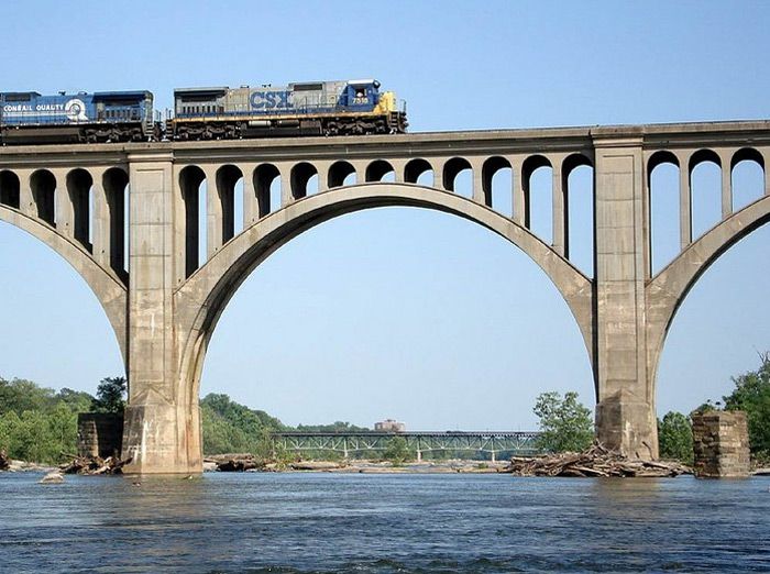 a train is crossing over the water on a bridge that has arches in it,