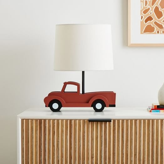 a red truck lamp sitting on top of a white table next to a wooden cabinet