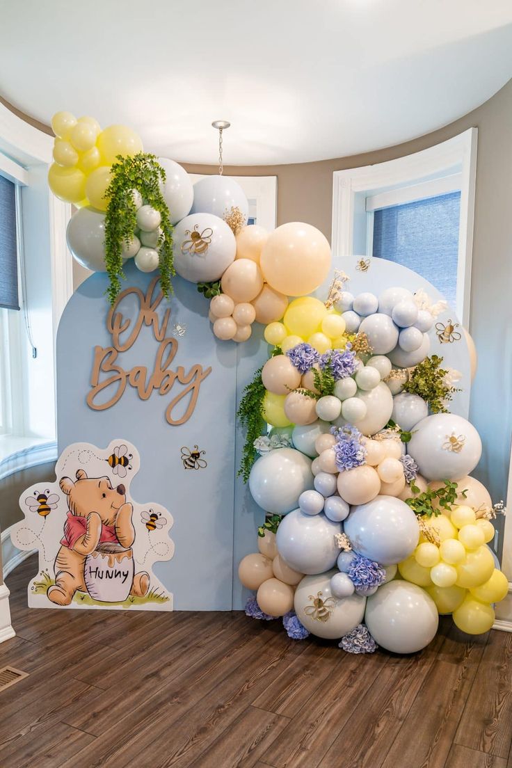 balloon arch for baby shower with winnie the pooh balloons and greenery on top