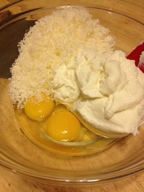 two eggs and coconut in a glass bowl on a wooden table with a red spatula