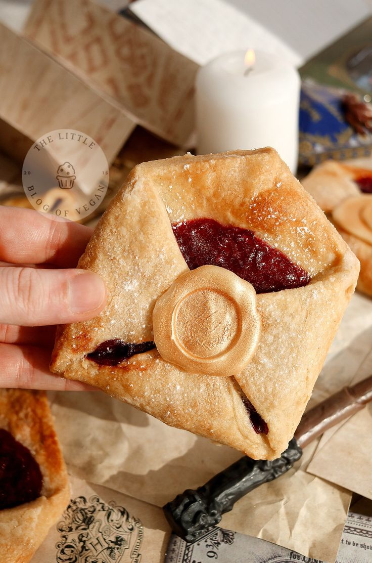 a hand holding a piece of food with jelly on it and other pastries in the background