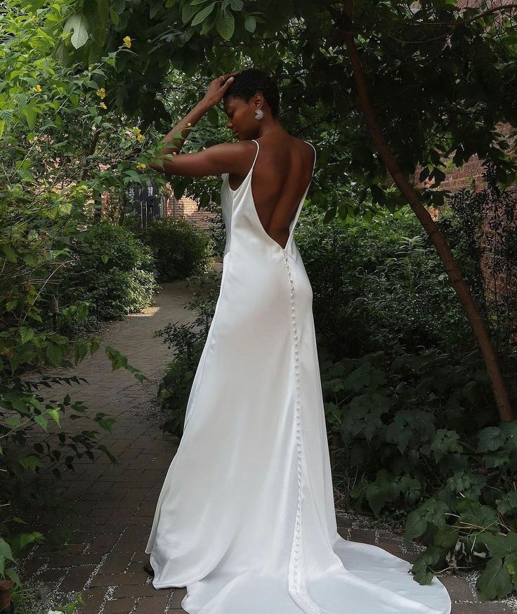 a woman in a white wedding dress standing under a tree with her back to the camera