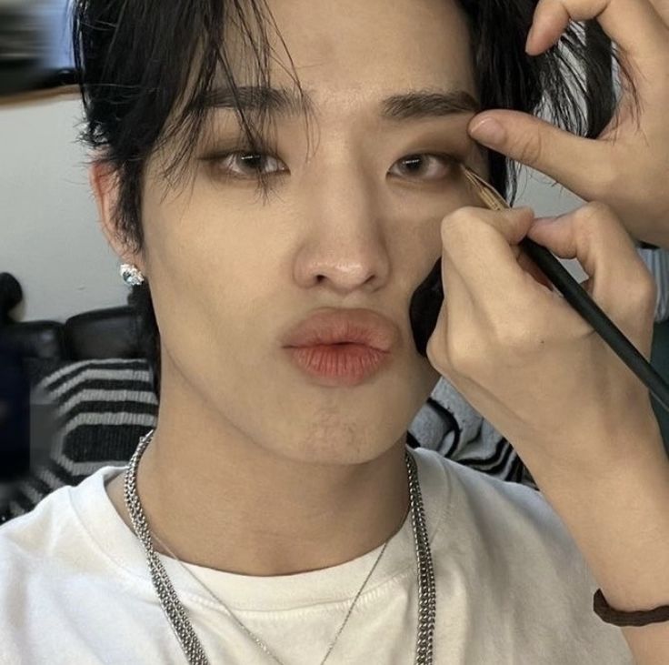 a young man is doing makeup on his face and holding a pencil in one hand