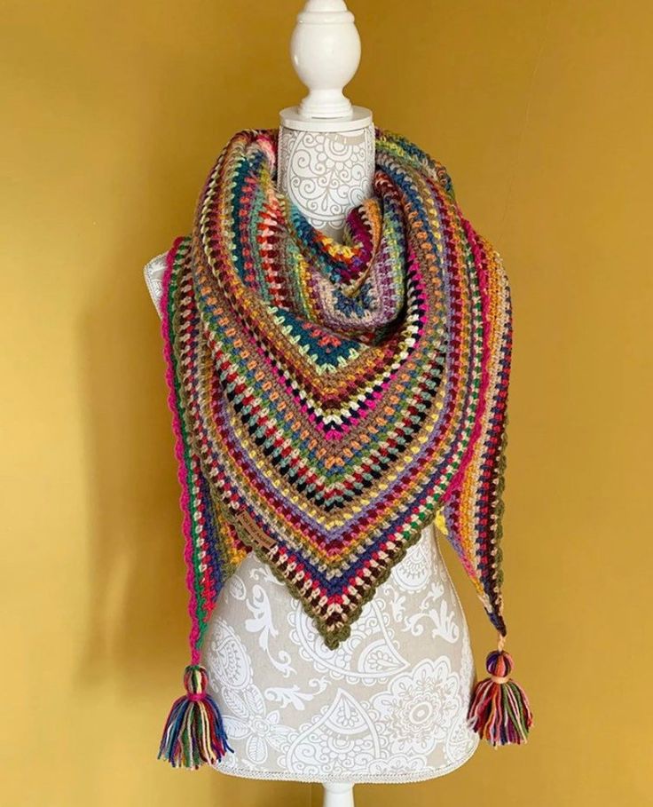 a white mannequin wearing a multicolored crocheted shawl with tassels