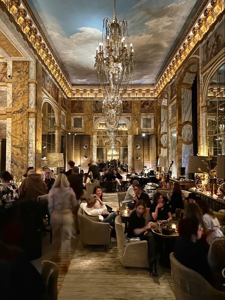 people sitting at tables in a fancy restaurant with chandelier and paintings on the ceiling