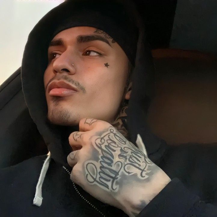 a man with tattoos on his arm sitting in a car wearing a black hoodie