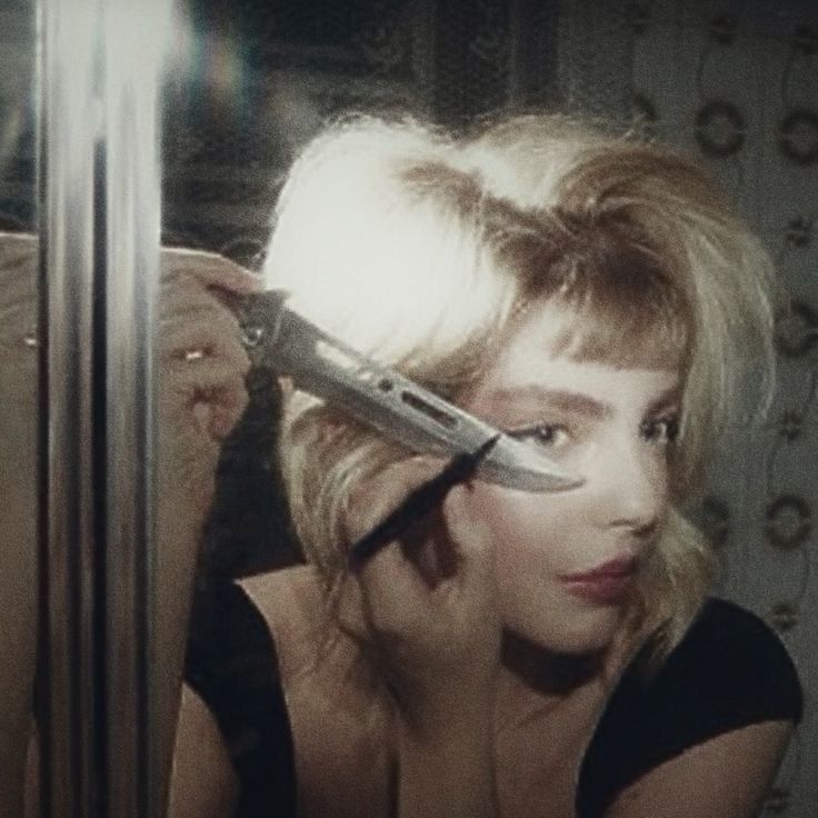 a woman is holding a knife in front of her face and looking into the mirror