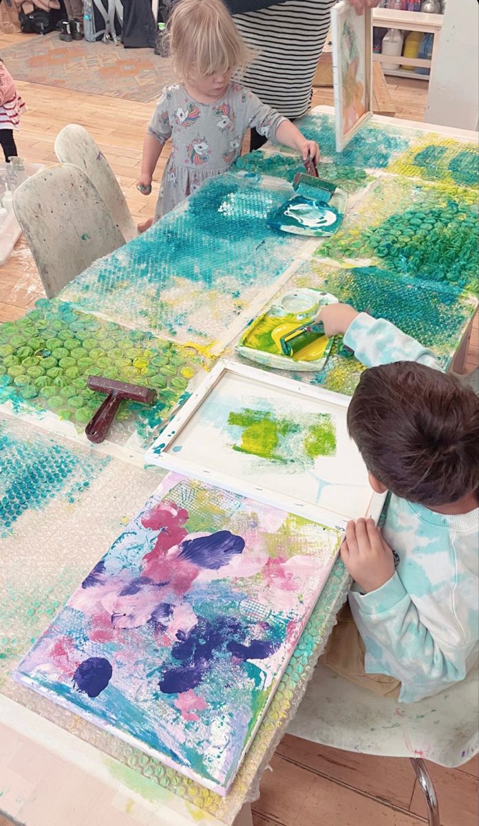 two children are painting on canvass at a table