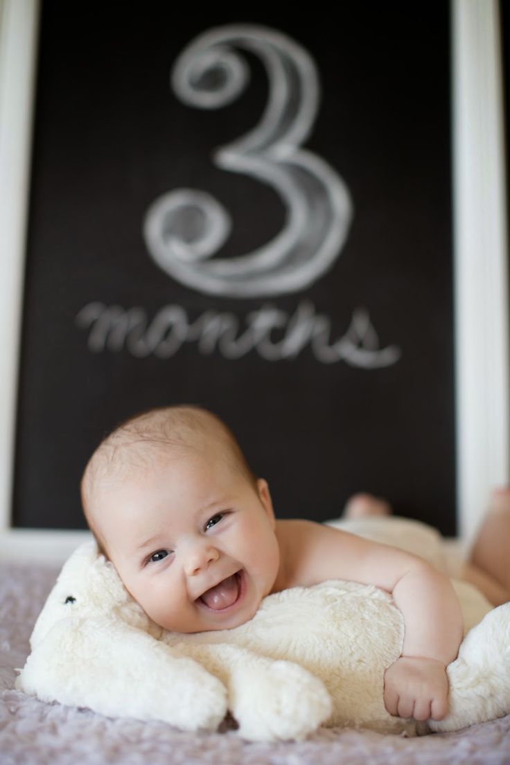 a smiling baby laying on top of a white teddy bear in front of a sign