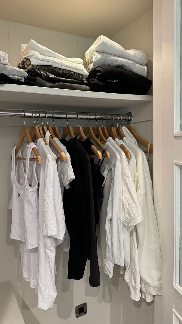 an organized closet with clothes hanging on the rails and folded white shirts in front of it