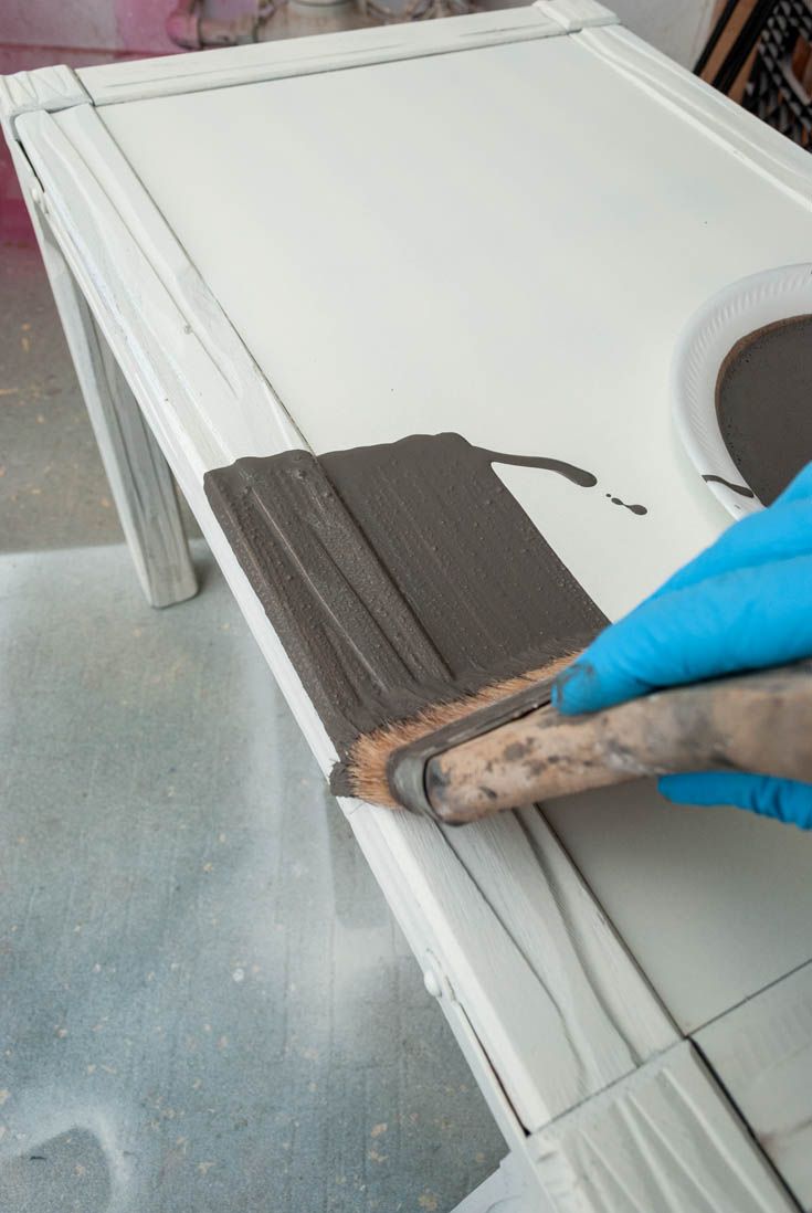 a person in blue gloves is painting a white table with black paint on the top