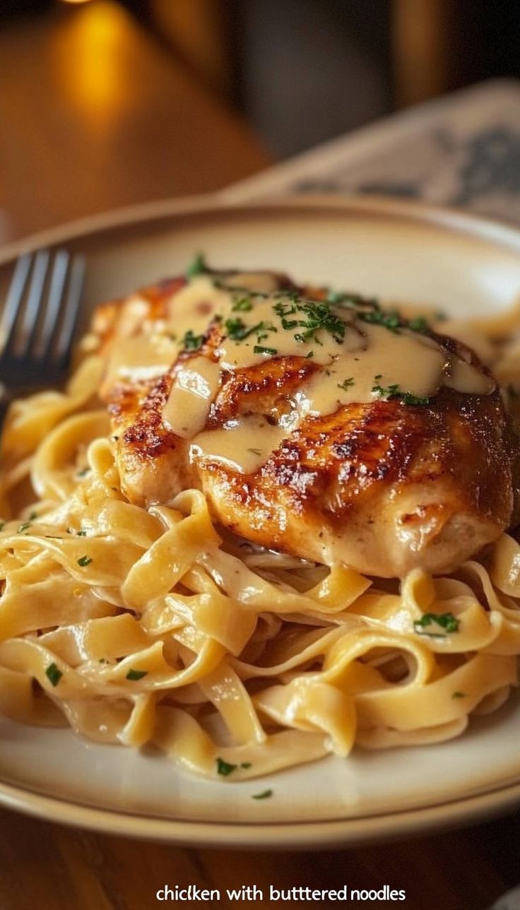 a white plate topped with chicken and pasta covered in gravy next to a fork