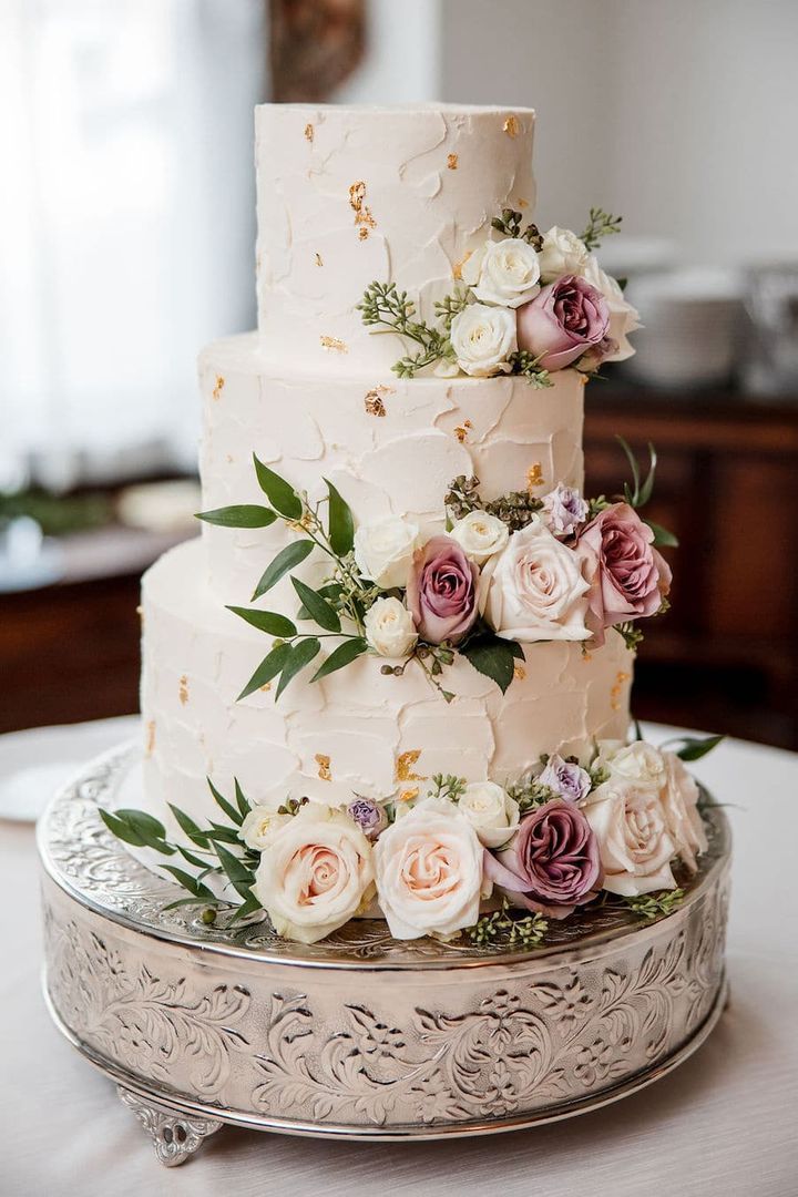 a three tiered wedding cake with pink and white flowers on the top is sitting on a silver platter