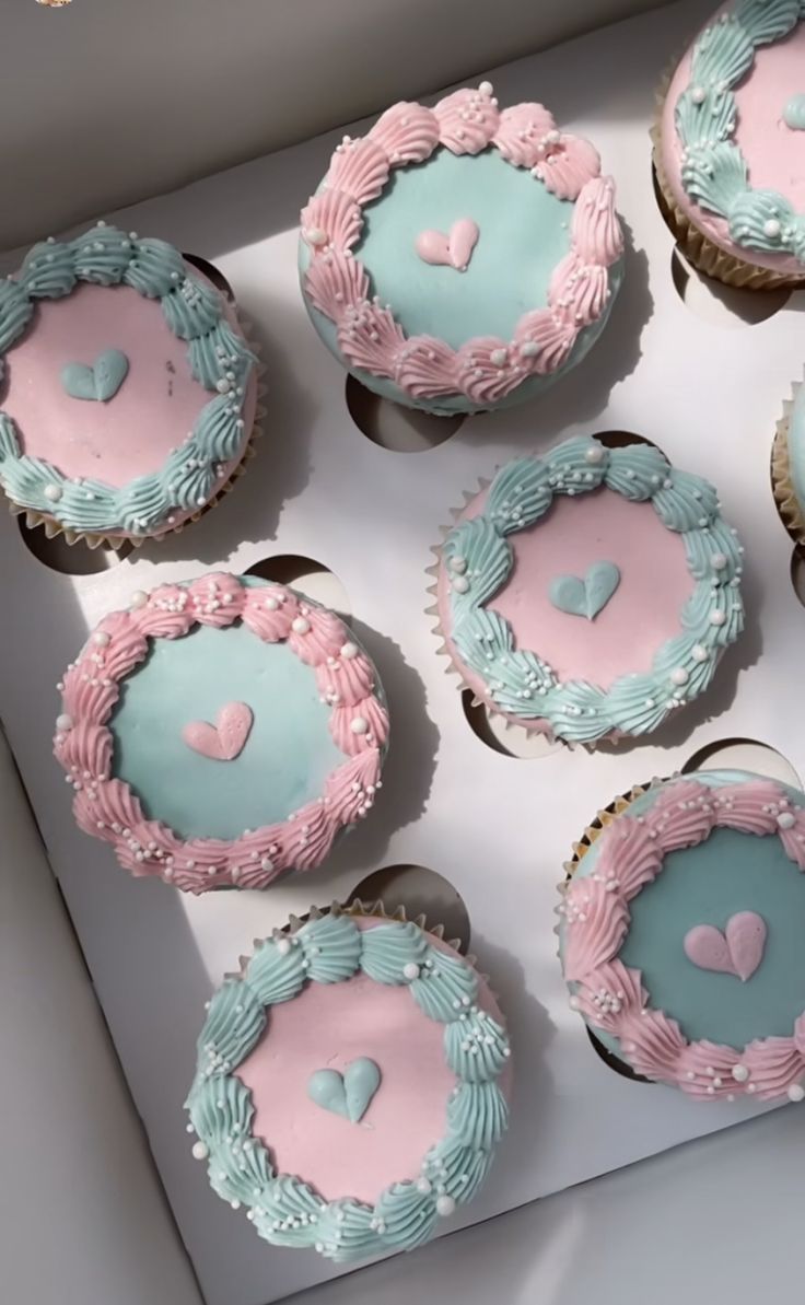 six cupcakes with pink and blue frosting in a box on a table