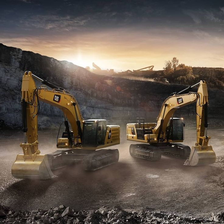 two yellow excavators are in the middle of a dirt field at sunset