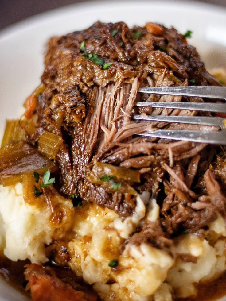 a white plate topped with meat and mashed potatoes covered in gravy next to a fork