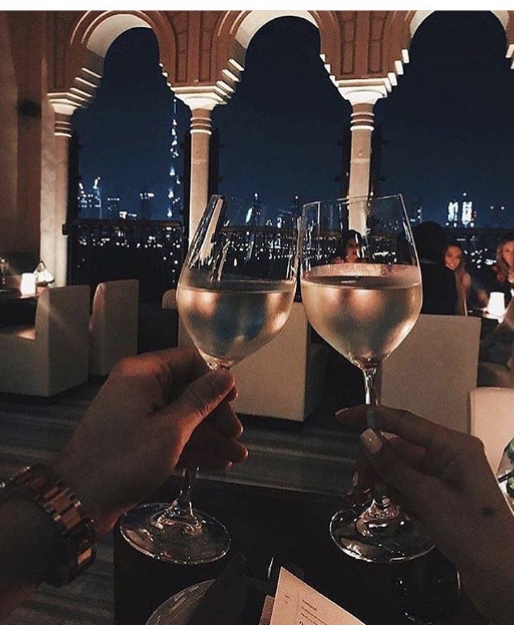 two people toasting with wine glasses in front of a cityscape at night