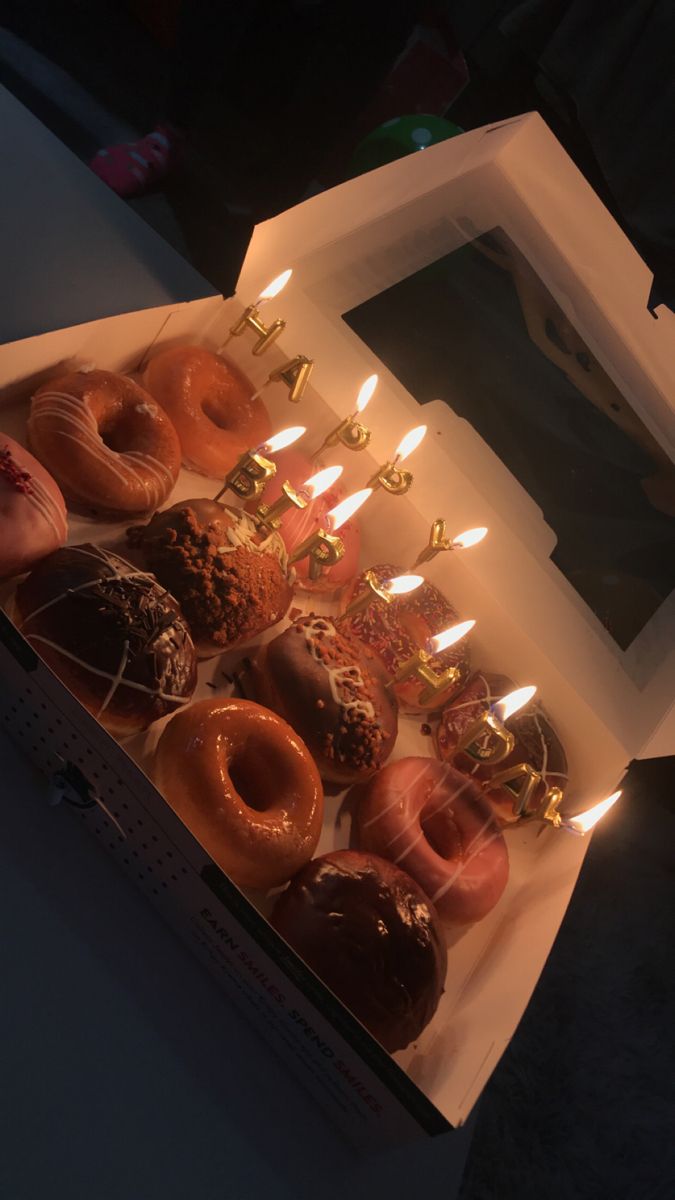 a box filled with lots of donuts sitting on top of a table next to candles