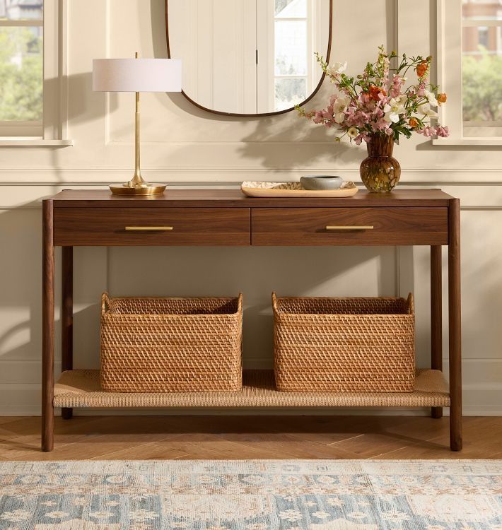 a console table with two baskets under a round mirror on the wall above it and a lamp next to it